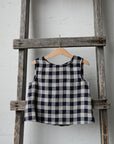 A blue and white checkered top is hanging on a wooden ladder against a white wall.