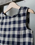 A blue and white checkered dress is hanging on a wooden hanger against a white wall.