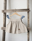 A beige dress with blue accents hangs on a wooden ladder against a white wall.