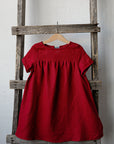 A red dress is hanging on a wooden ladder against a white wall.