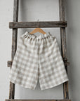 A pair of gray and white checkered shorts is hanging on a wooden ladder against a white wall.