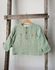 A light green button-down shirt is hanging on a wooden ladder against a white wall.