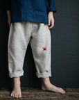 A person wearing a blue shirt and gray pants with a red crab embroidered on the front, standing on a wooden surface against a dark background.