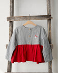 A gray and red striped jacket is hanging on a wooden ladder against a white wall.