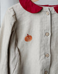 A light-colored dress with a red collar and a small orange pumpkin embroidered on the front.