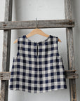 A blue and white checkered dress is hanging on a wooden ladder against a white wall.
