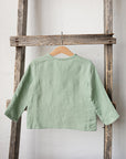 A light green, long-sleeved shirt is hanging on a wooden ladder against a white wall.