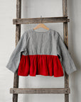 A gray and red striped blouse is hanging on a wooden ladder against a white wall.