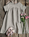 a gray dress with a ribbon, pink shoes, and pink roses arranged on a wooden surface.