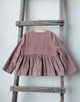 A pink ruffled jacket is hanging on a wooden ladder against a white wall.