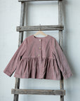 A pink ruffled jacket is hanging on a wooden ladder against a white wall.