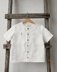 A white button-down shirt is hanging on a wooden ladder against a white wall.