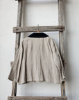 A beige jacket with a black collar is hanging on a wooden ladder against a white wall.