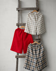 Three pairs of men's shorts hanging on a wooden ladder against a white wall.