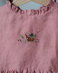 A pink dress with a small embroidered design of a rabbit and flowers on the front.