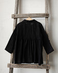 A black jacket is hanging on a wooden ladder against a white wall.
