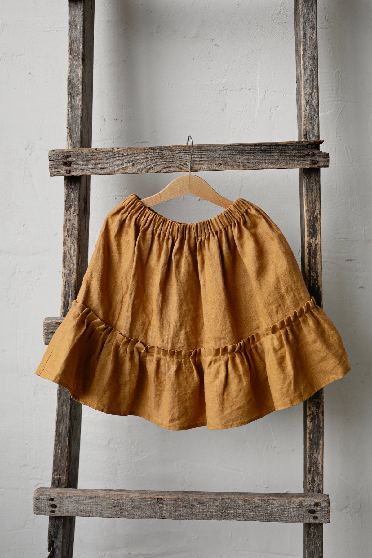 A yellow ruffled skirt is hanging on a wooden ladder against a white wall.