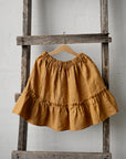 A yellow ruffled skirt is hanging on a wooden ladder against a white wall.