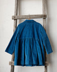 A blue corduroy dress is hanging on a wooden ladder against a white wall.