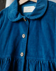 A blue dress with a button-down collar and ruffled hem, hanging on a wooden hanger.