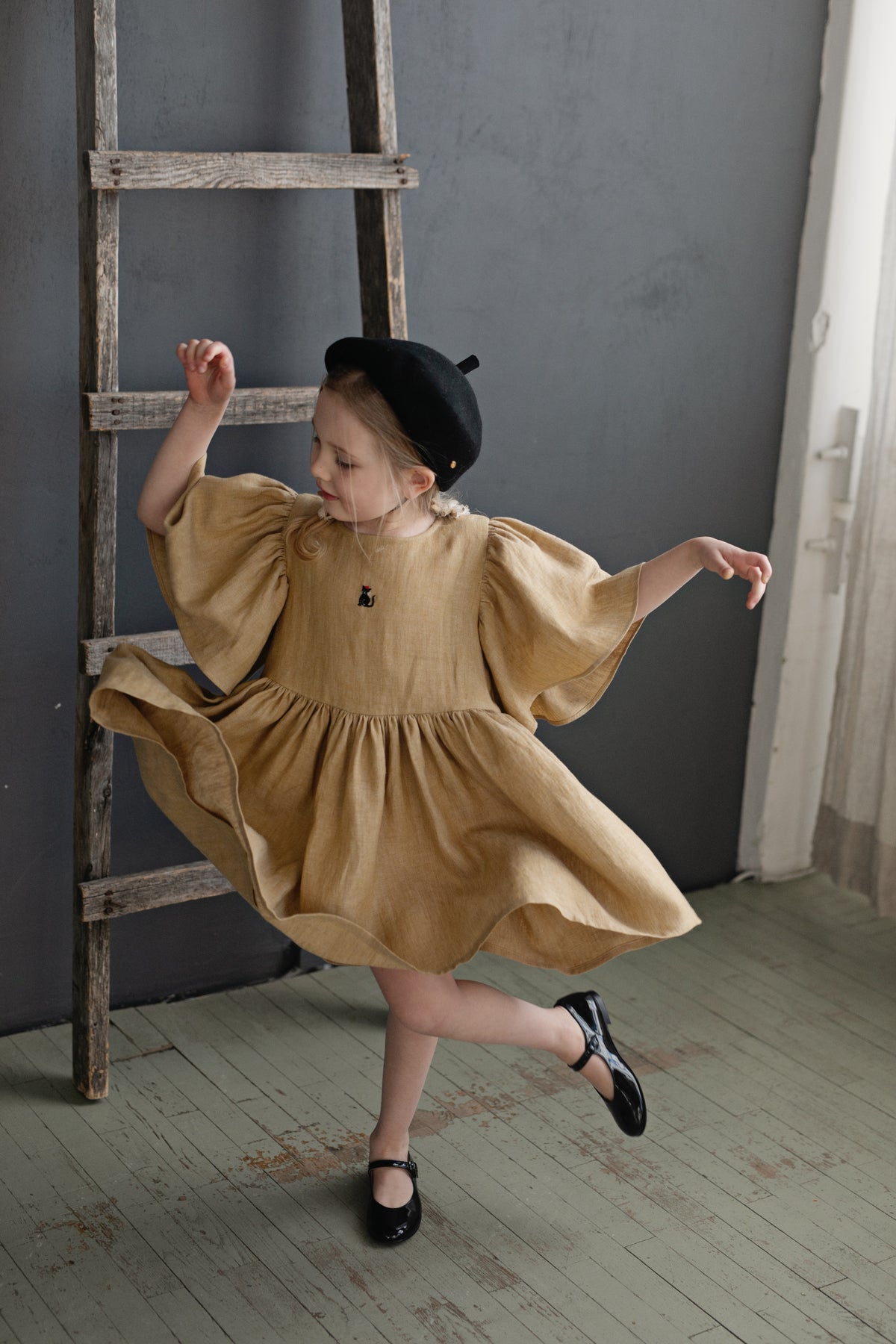 a little girl in a brown dress and black hat