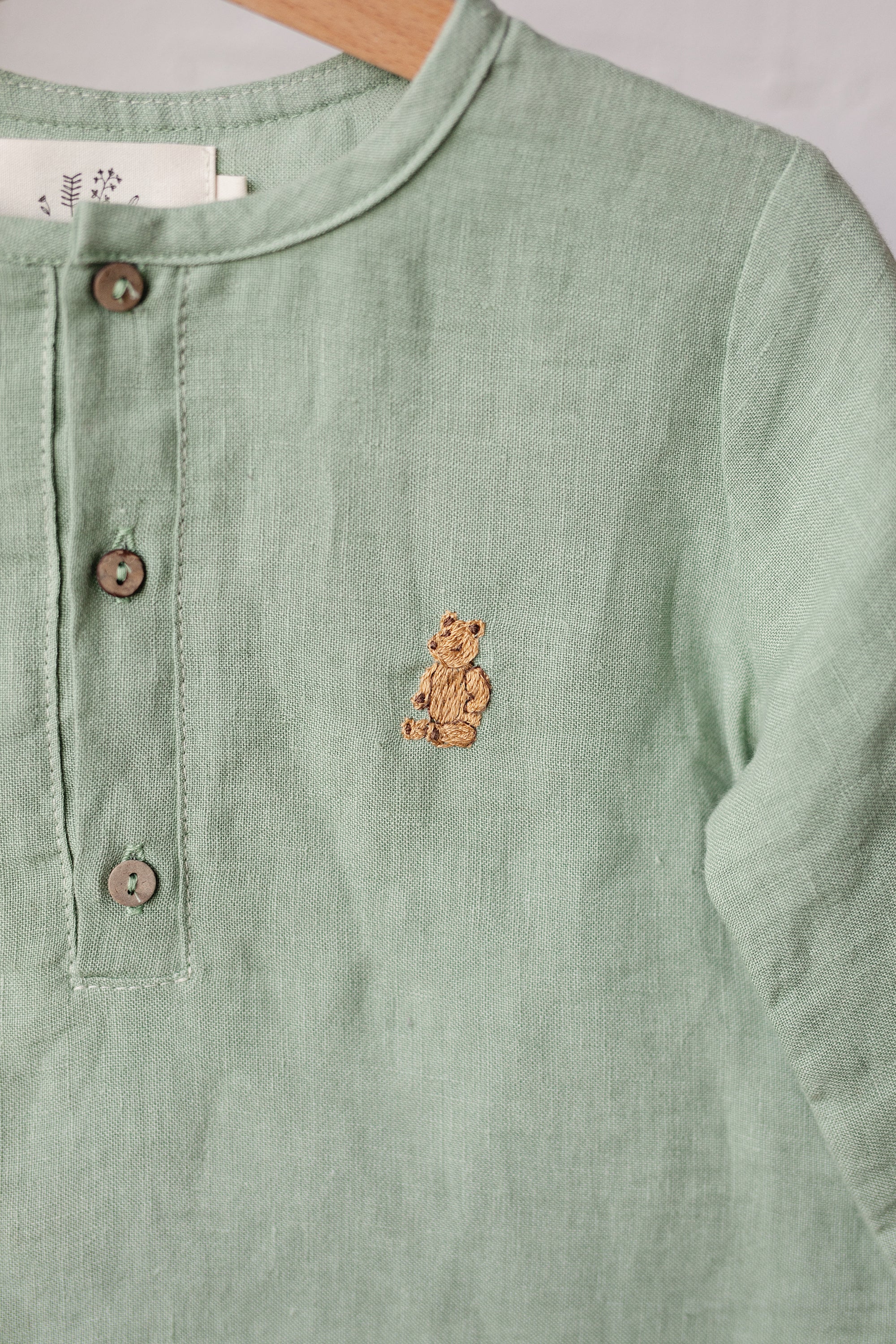 A light green button-down shirt with a small embroidered teddy bear design on the front.