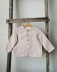 A pink polka dot shirt is hanging on a wooden ladder against a white wall.