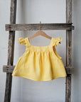 A yellow dress with ruffled sleeves is hanging on a wooden ladder against a white wall.