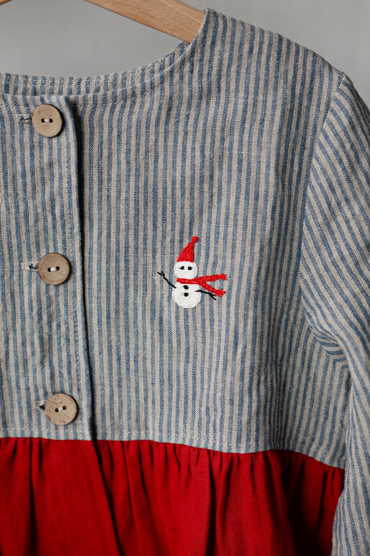A close-up view of a striped dress with a red skirt and a small snowman embroidered on the front.