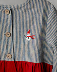 A close-up view of a striped dress with a red skirt and a small snowman embroidered on the front.