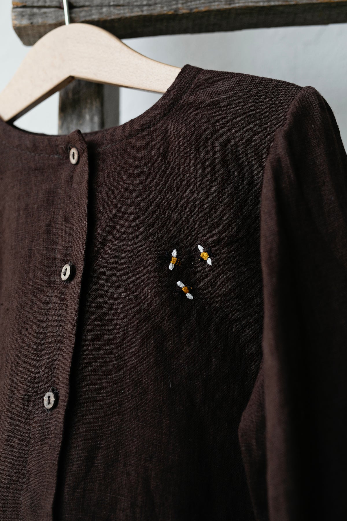 A brown button-up shirt with a small embroidered bee design on the front.