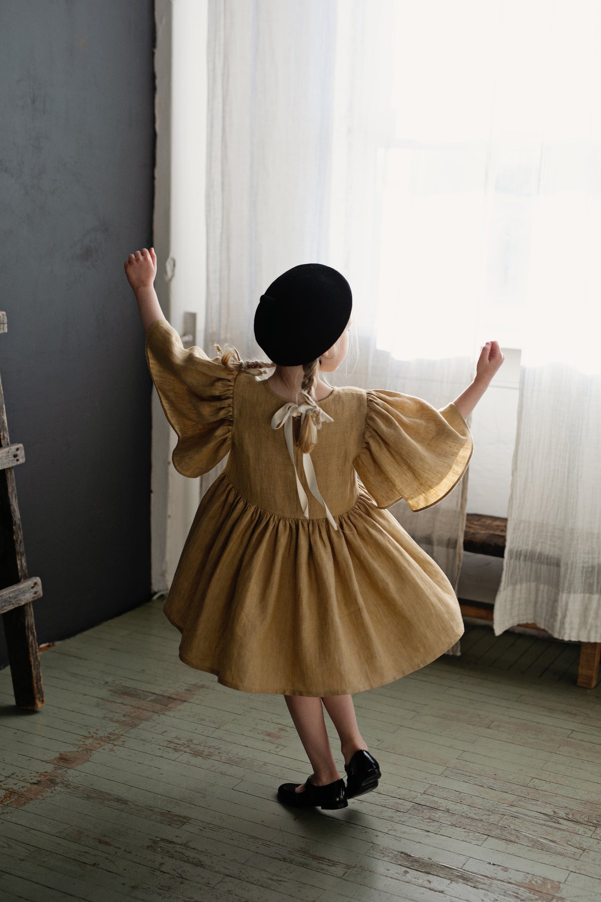 a little girl in a brown dress and black hat
