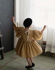 a little girl in a brown dress and black hat