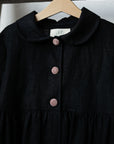 A black dress with a ruffled collar and three buttons, hanging on a wooden hanger.