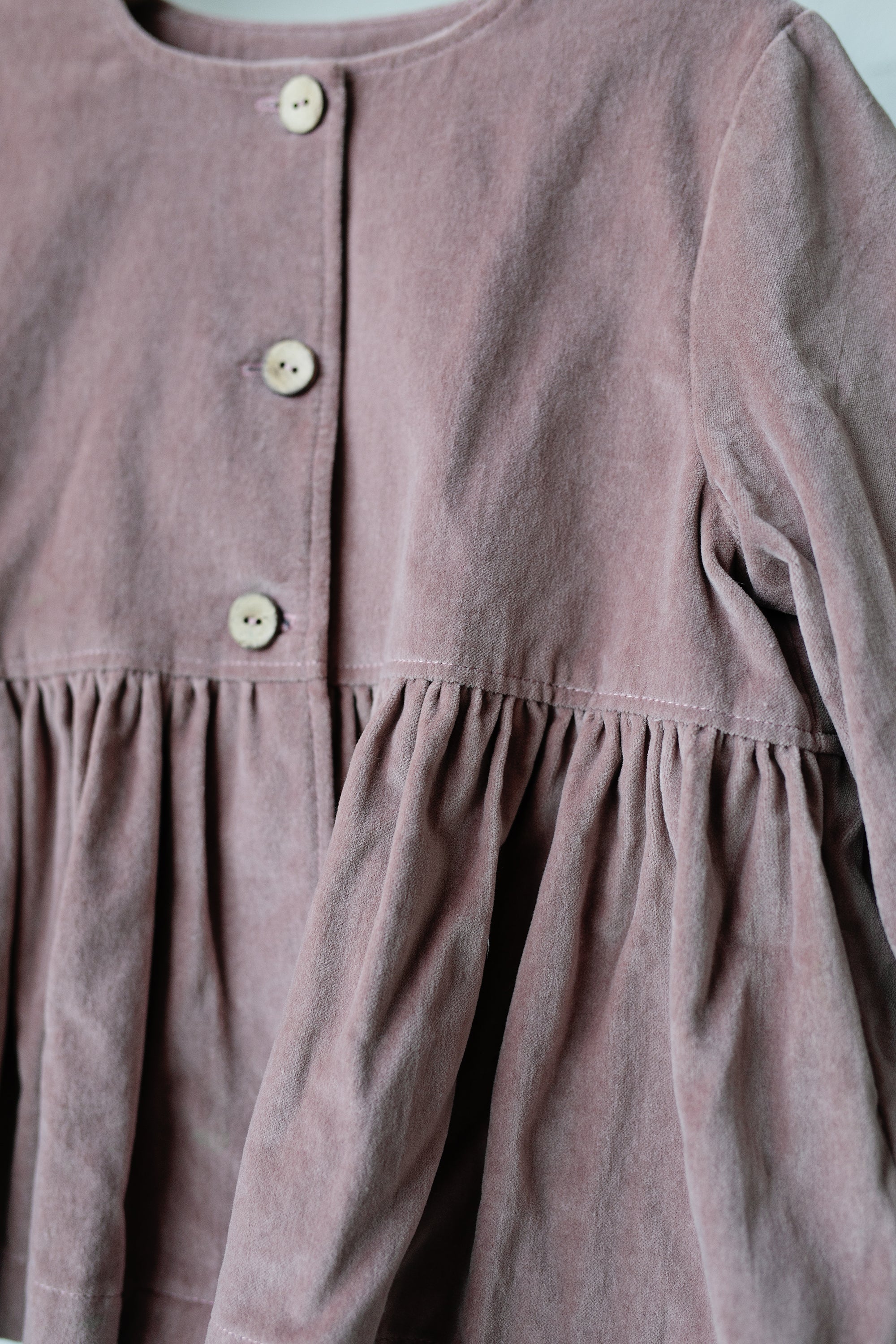 A close-up view of a pink fabric with a ruffled collar and three buttons.
