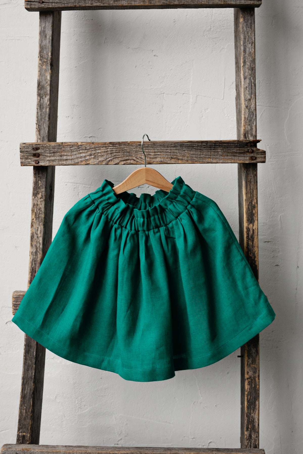 A green skirt is hanging on a wooden ladder against a white wall.