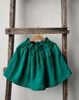 A green skirt is hanging on a wooden ladder against a white wall.