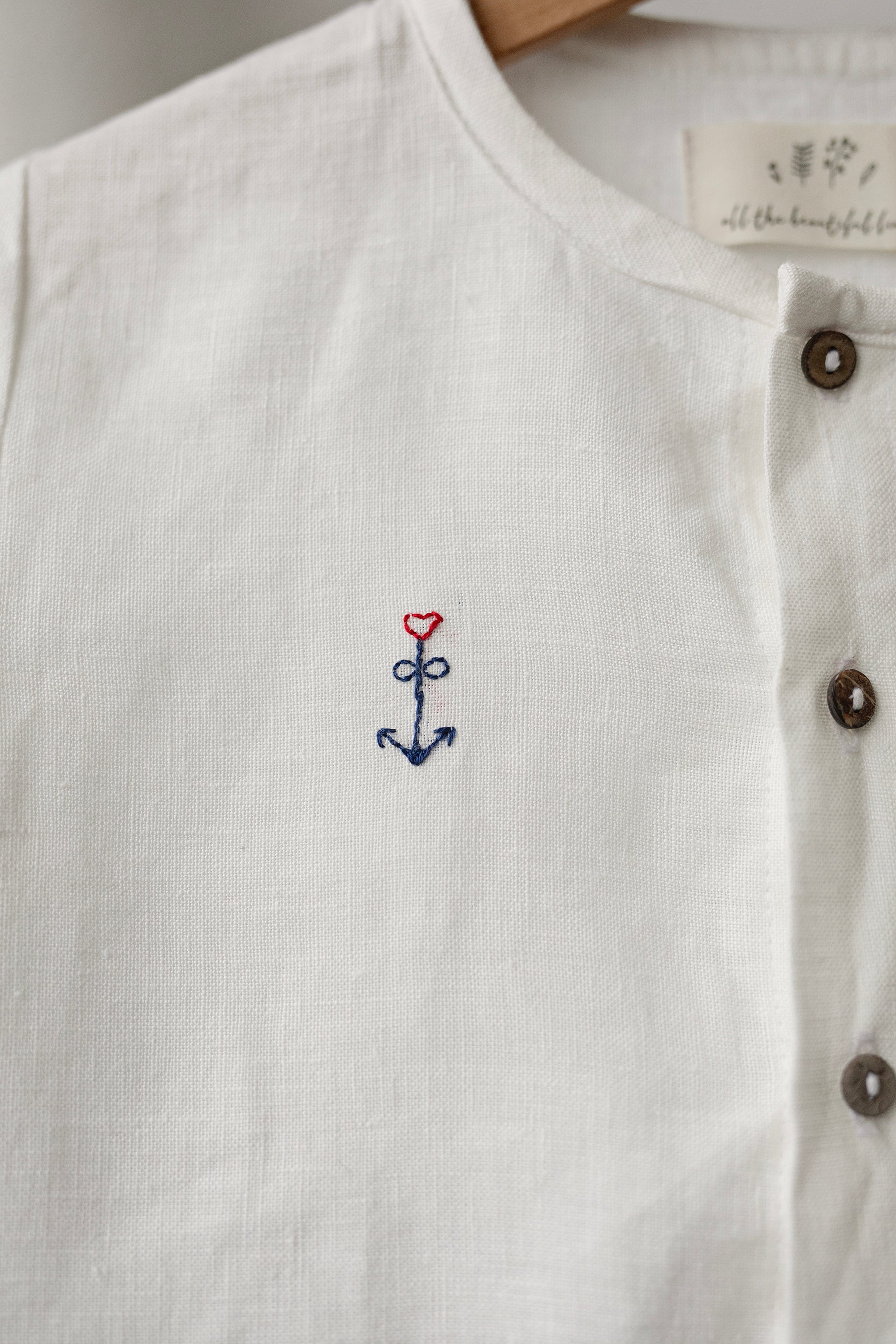 A close-up view of a white shirt with a small embroidered anchor symbol on the front.