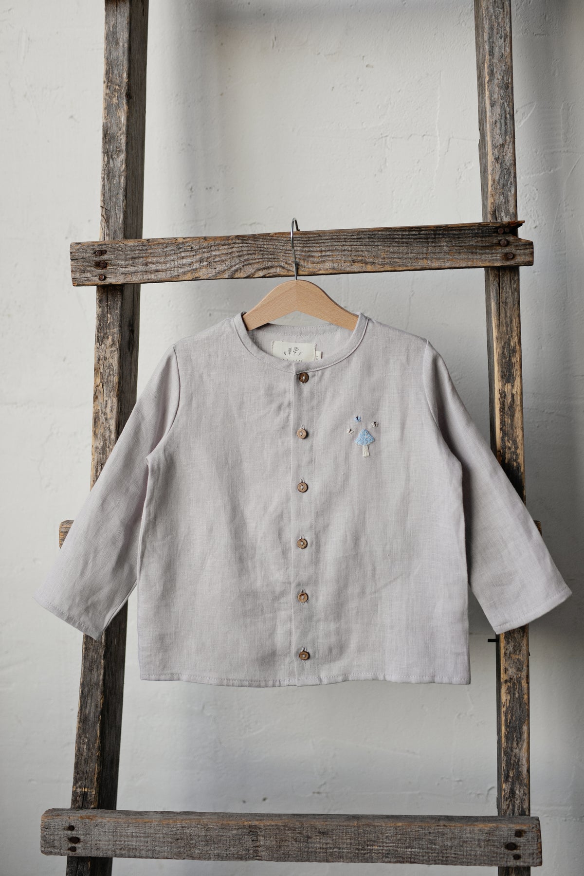 A light gray button-up shirt is hanging on a wooden ladder against a white wall.