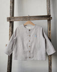 A light gray button-up shirt is hanging on a wooden ladder against a white wall.