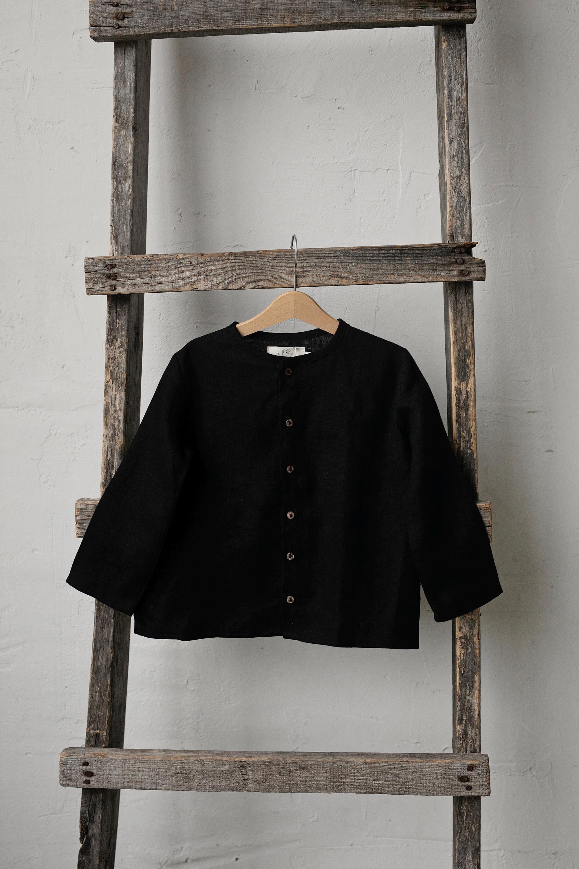 A black button-up shirt is hanging on a wooden ladder against a white wall.