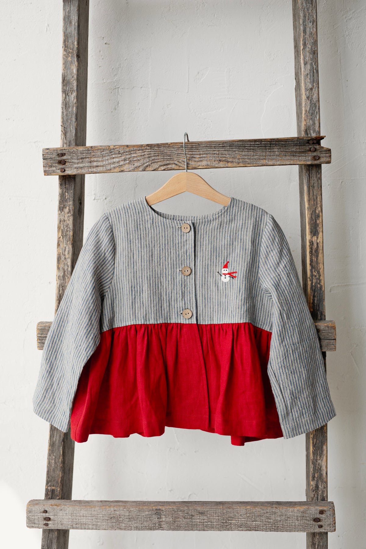 A gray and red striped jacket is hanging on a wooden ladder against a white wall.