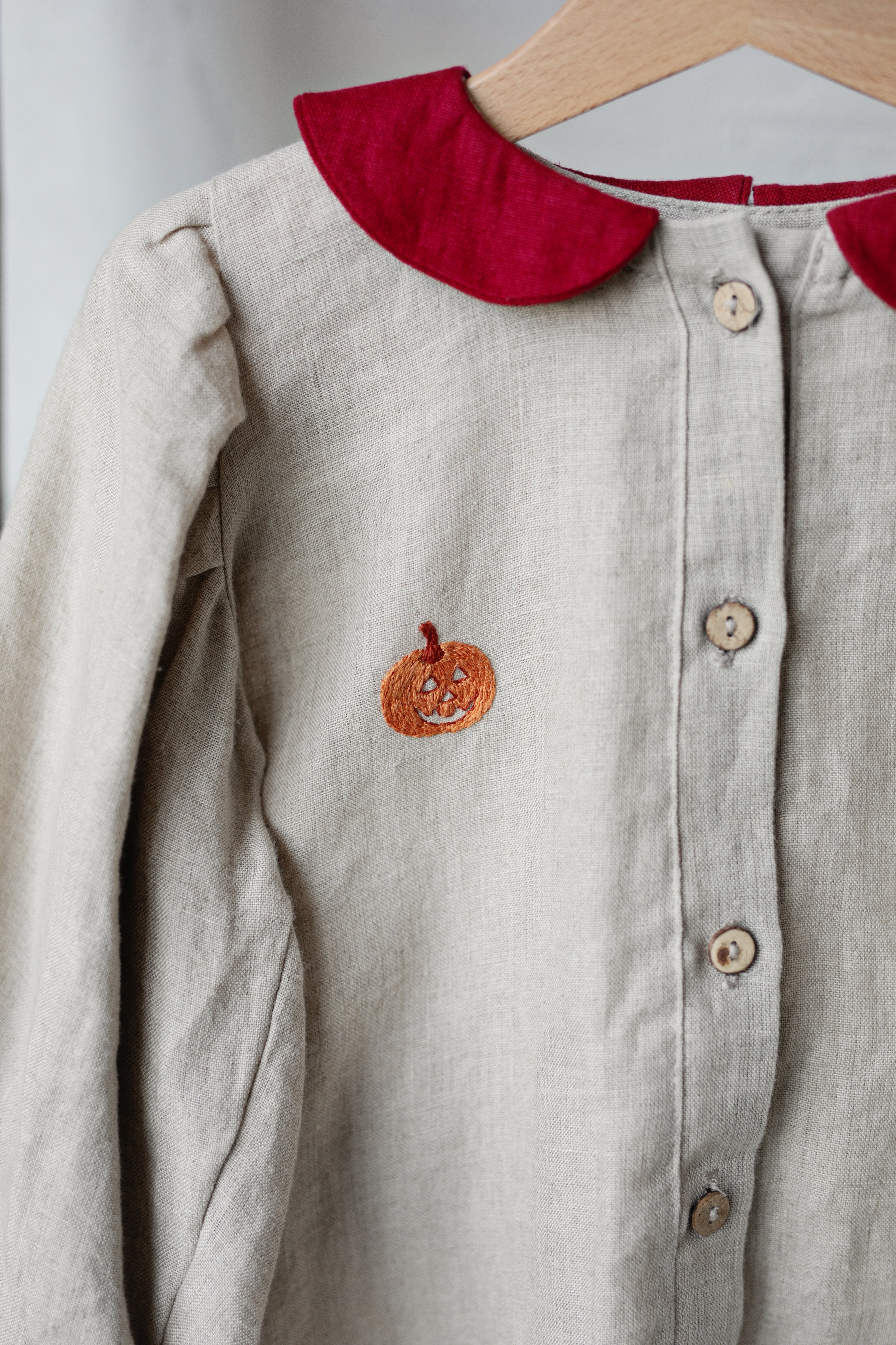 A light-colored dress with a red collar and a small orange pumpkin embroidered on the front.