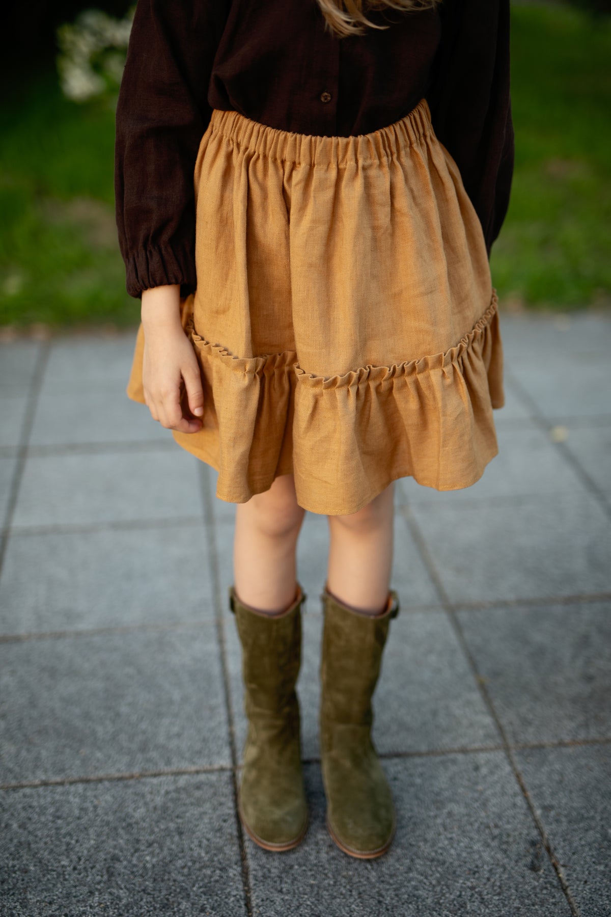 A person wearing a brown top, a yellow skirt, and green boots stands on a tiled surface.