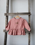 A pink ruffled dress is hanging on a wooden ladder against a white wall.