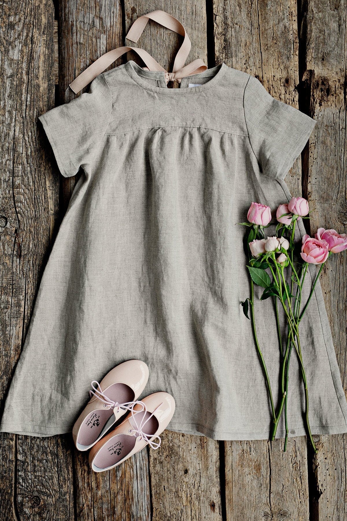 a gray dress with a ribbon, pink shoes, and pink roses arranged on a wooden surface.
