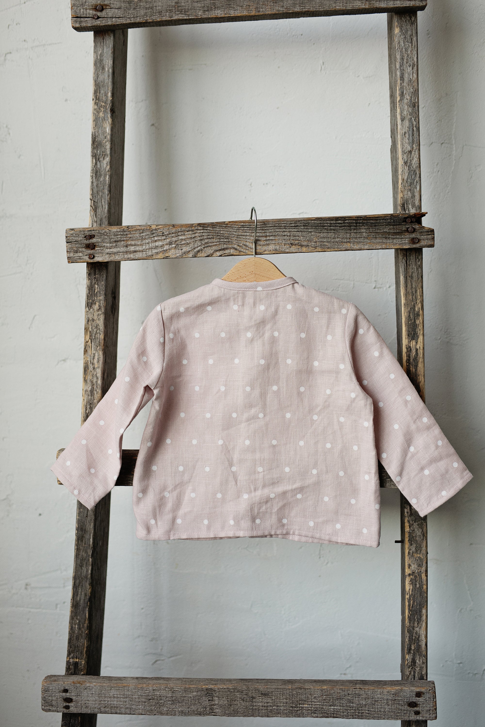 A wooden ladder with a pink polka dot shirt hanging from one of the rungs.