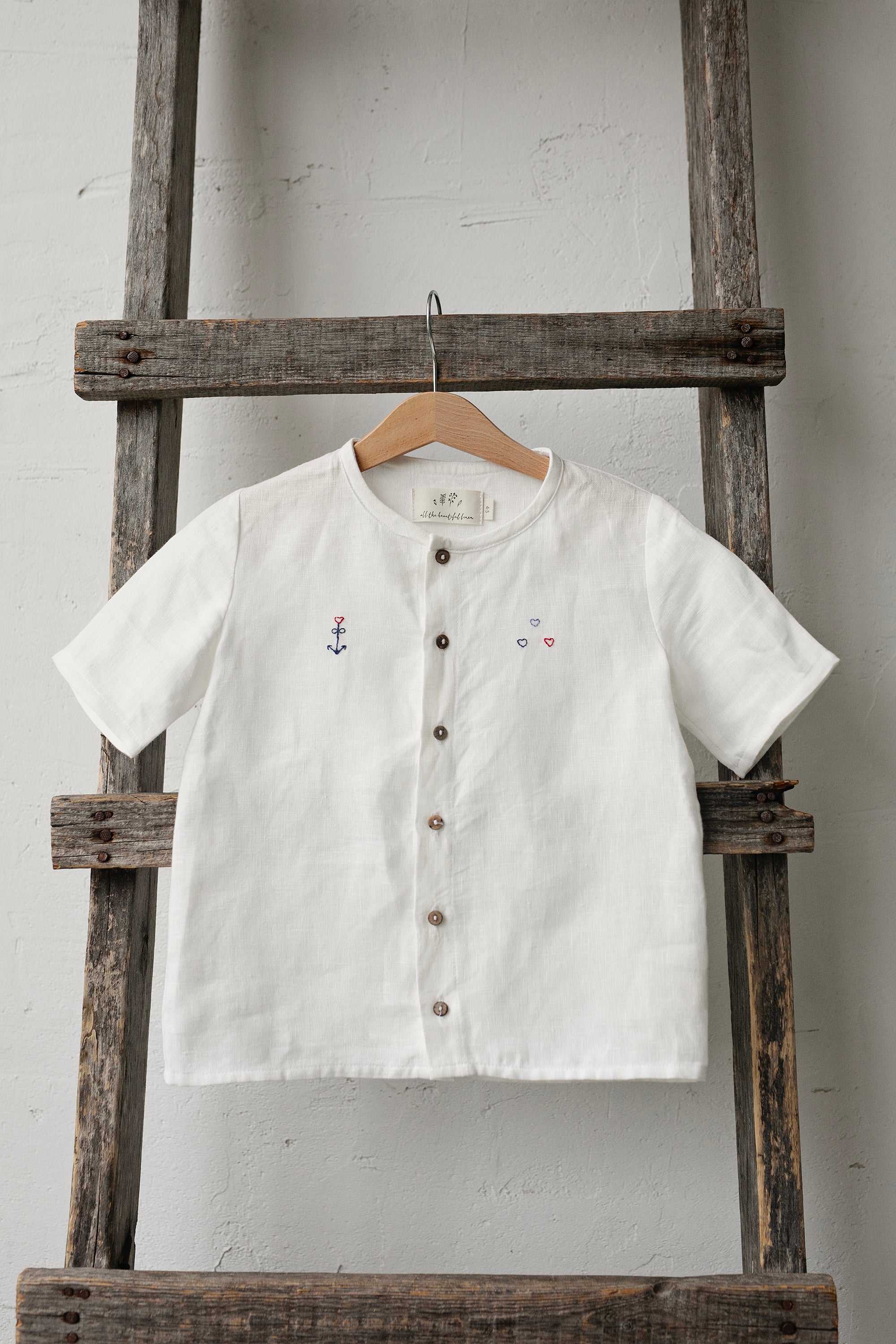 A white button-down shirt is hanging on a wooden ladder against a white wall.