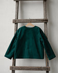 A dark green long-sleeved shirt is hanging on a wooden ladder against a white wall.
