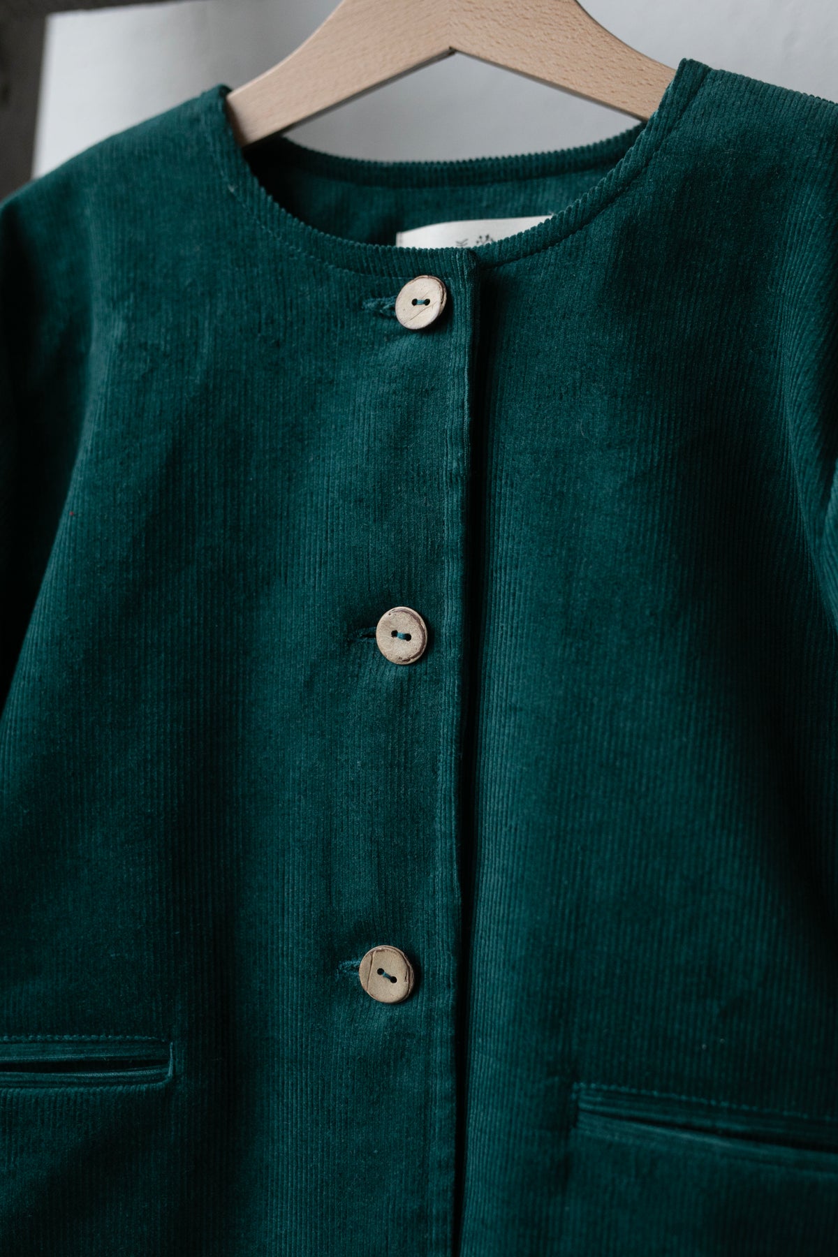 A close-up view of a dark green button-down jacket with three buttons and two pockets.